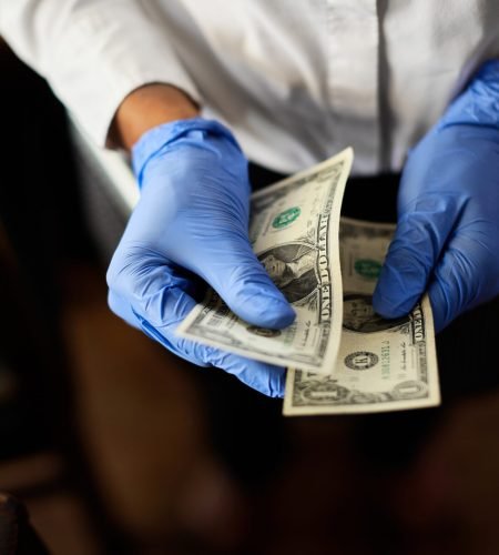 Close-up of waitress wearing protective gloves while counting money in a cafe.